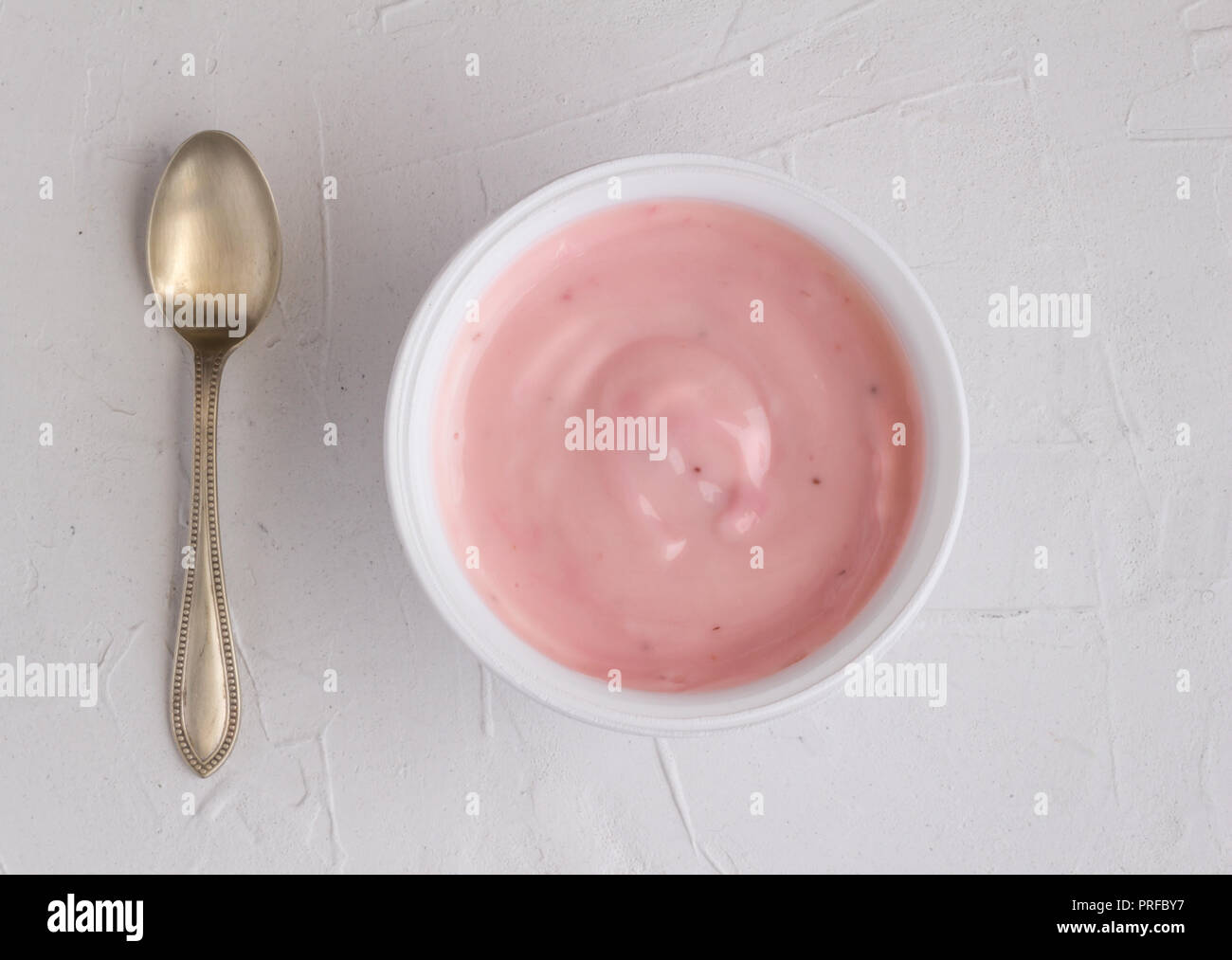 Yoghurt cup with pink strawberry yogurt on grey background with small silver spoon Stock Photo