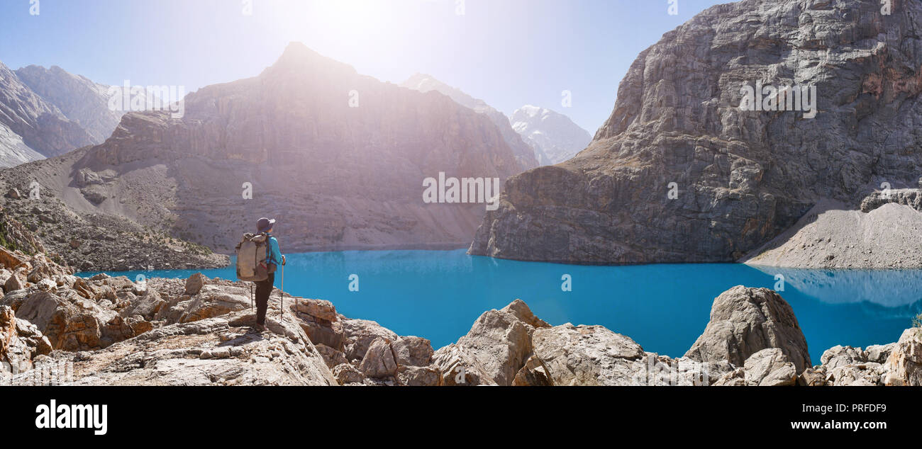 Girl with backpack near lake Big Alo on rocky mountain background. Fann Mountains, Tajikistan, Central Asia Stock Photo