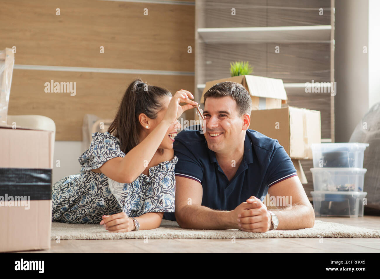 Happy new flat couple of owners showing keys sitting in the floor. Moving in day. Stock Photo