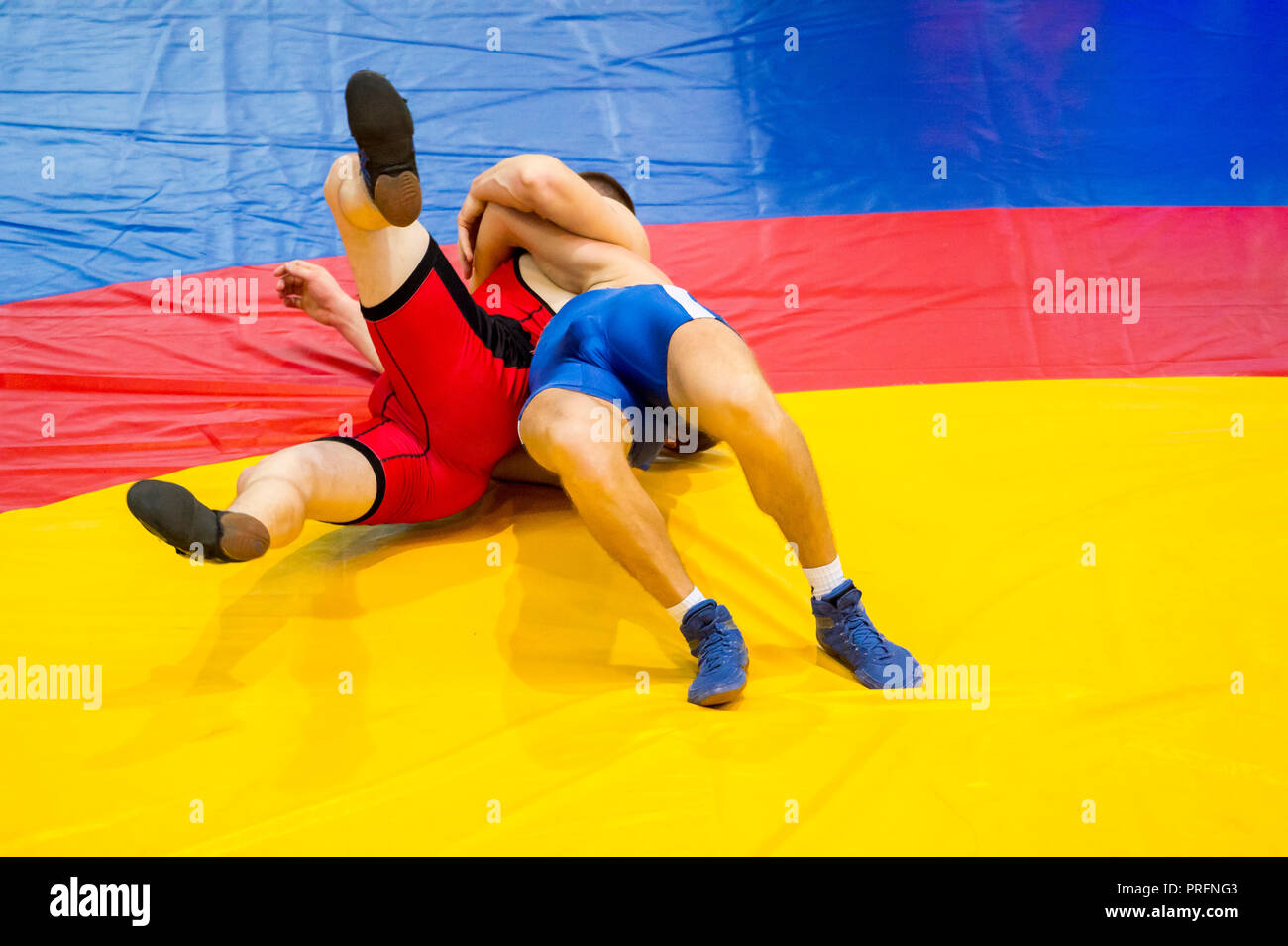 Two young men in blue and red wrestling on a yellow wrestling carpet in