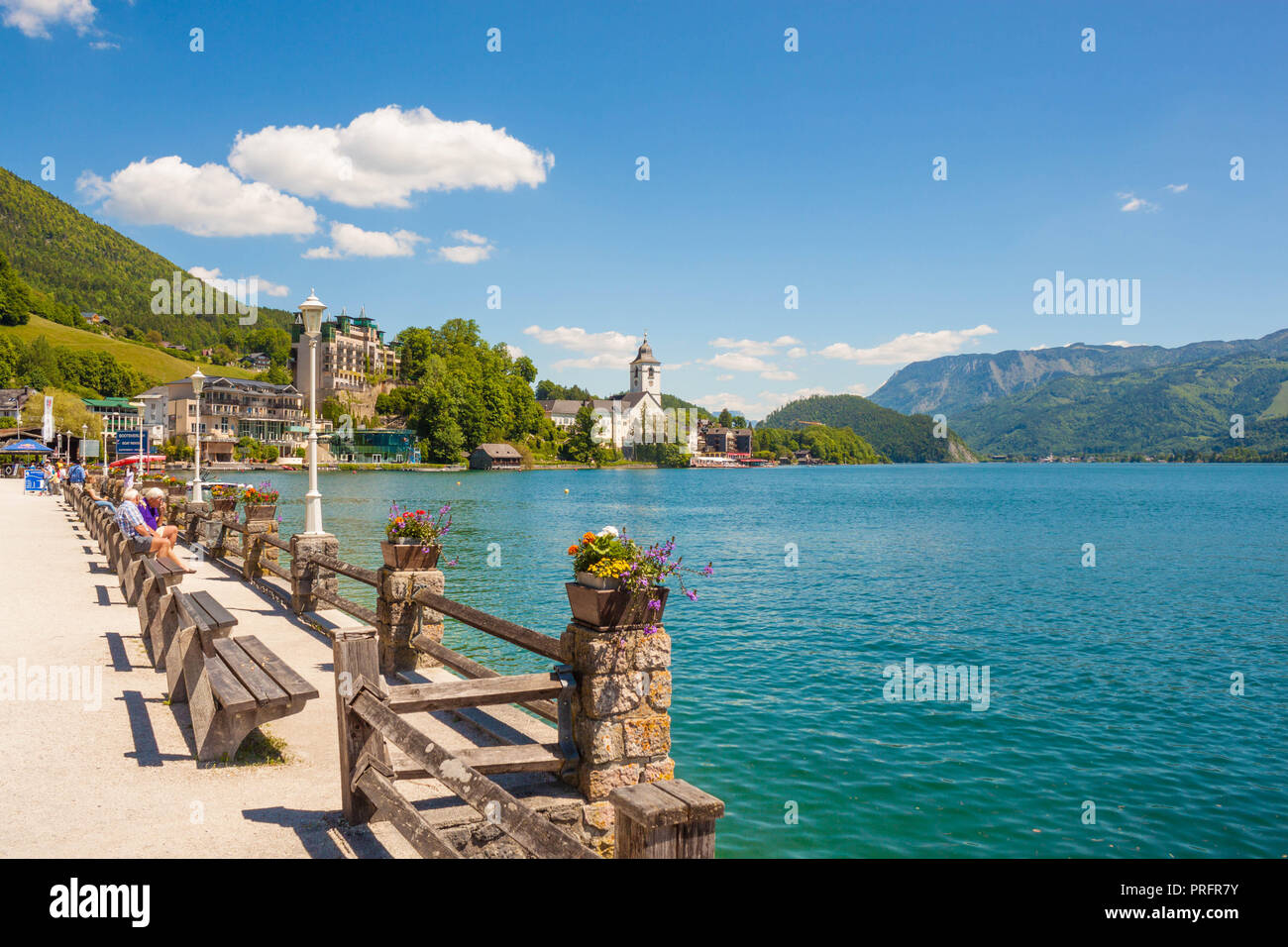 St. Wolfgang, Austria - May 27, 2017: Waterfront promenade on alpine lake Wolfgangsee with a row of wooden benches. View of St.Wolfgang church  and mo Stock Photo