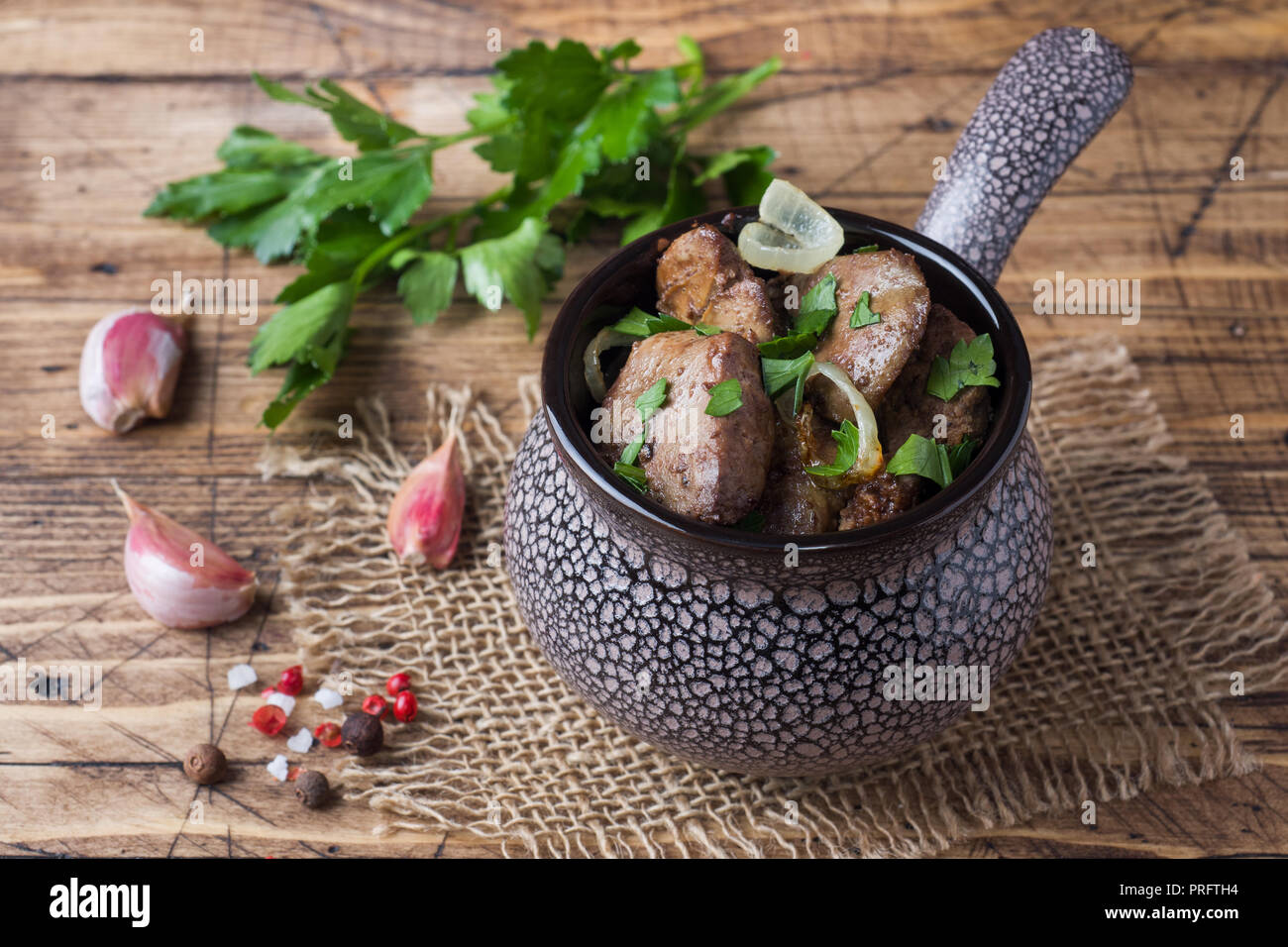 Baked chicken liver with onion in a ceramic cocotte on a wooden rustic