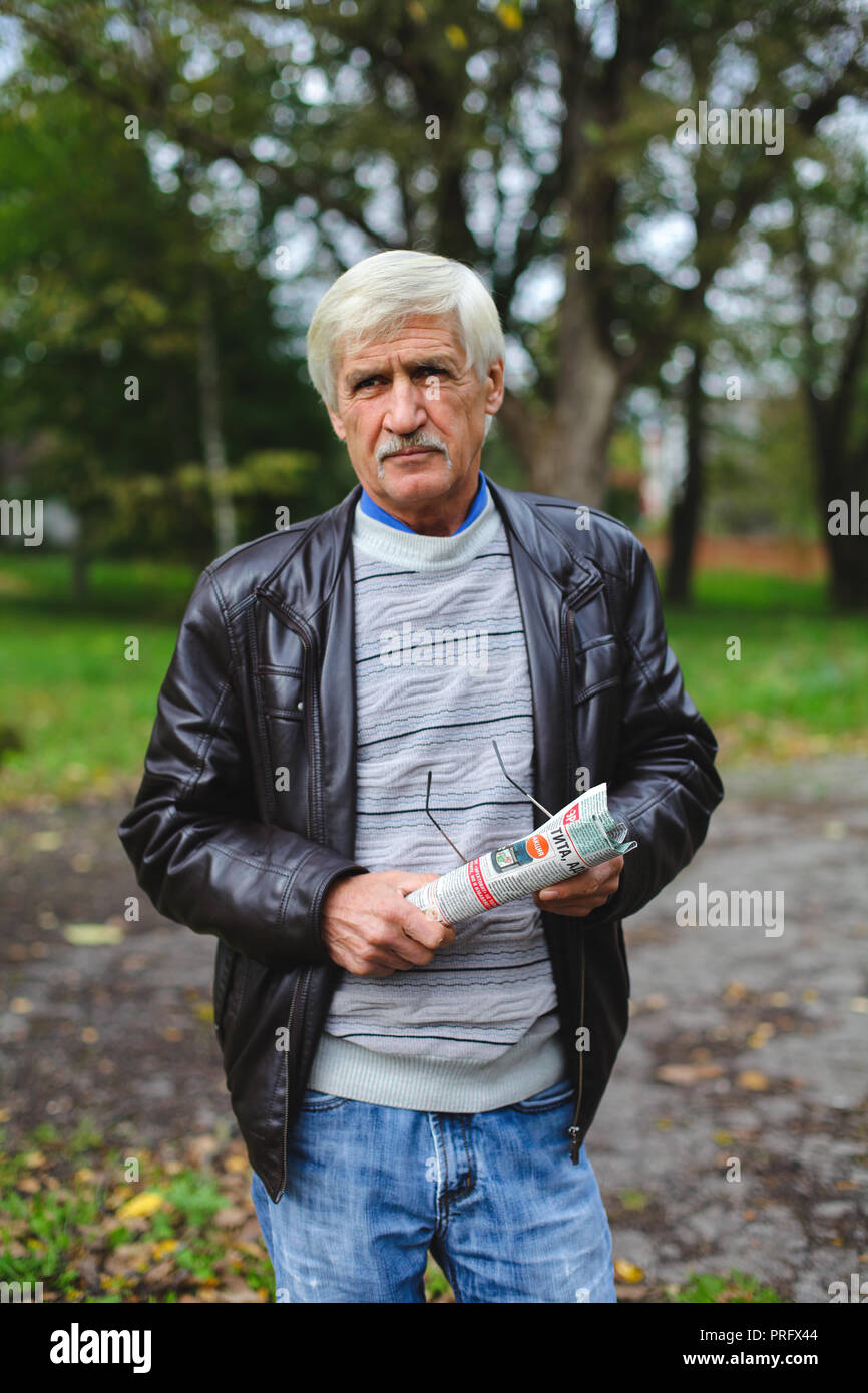 a portrait of a gray man is 60 years old. He holds a newspaper in his hands. The man has poor eyesight, he is wearing glasses Stock Photo