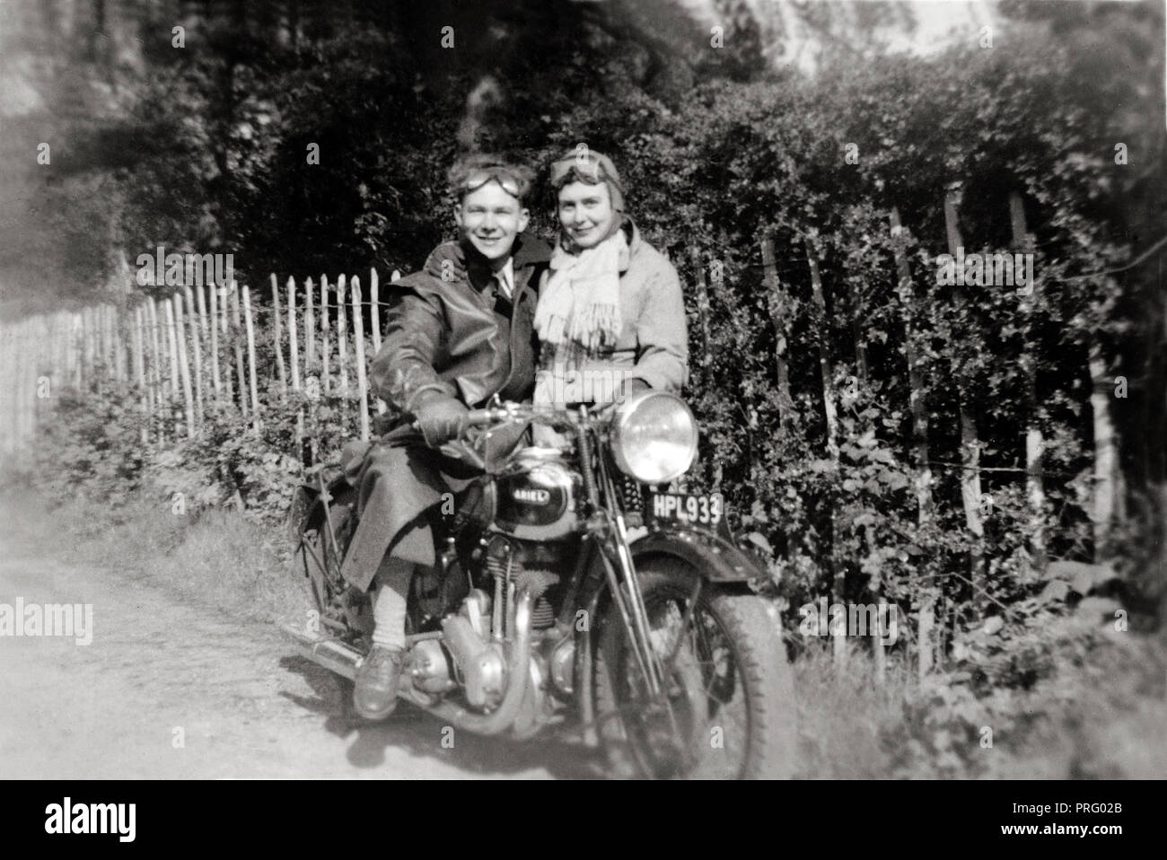 Man on 1938 Ariel Red Hunter motorcycle with woman standing beside him country lane circa 1938 Stock Photo