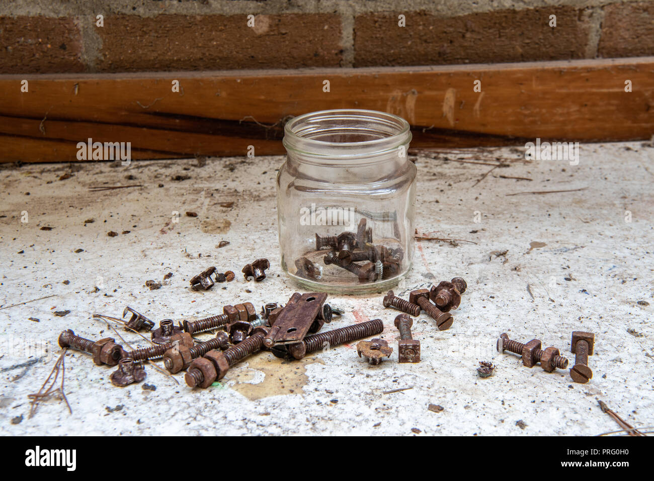 Jar of rusty bolts, nuts, hinges and washers on a workshop bench. Stock Photo