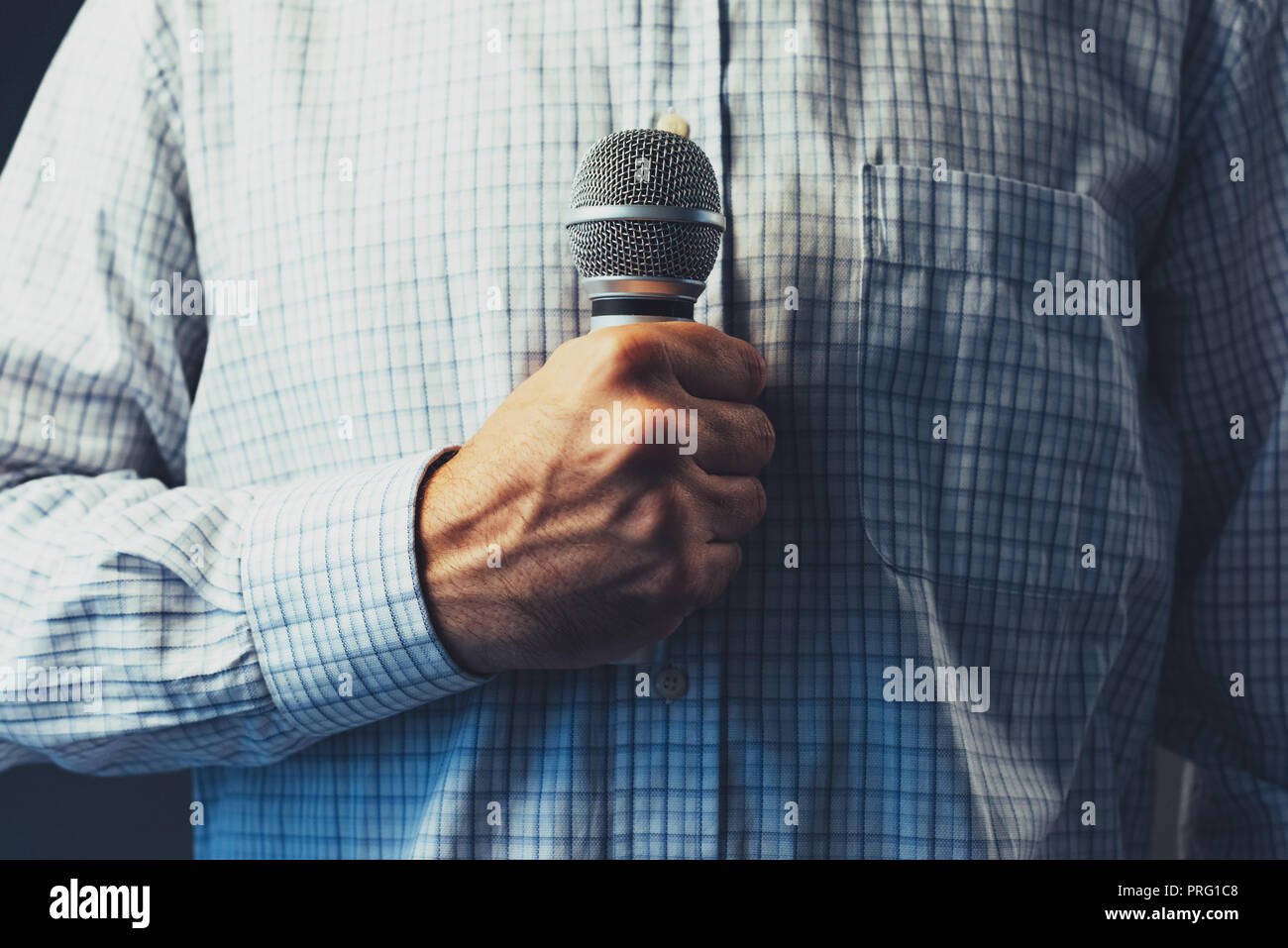 Public speaker holding microphone, low key with selective focus Stock Photo