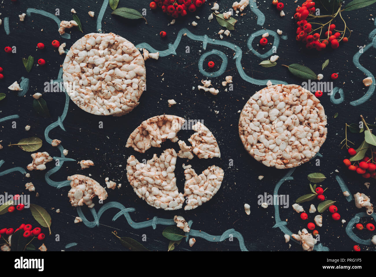 Flat lay crunchy rice cakes on dark wooden background with floral arrangement background, overhead top down view Stock Photo