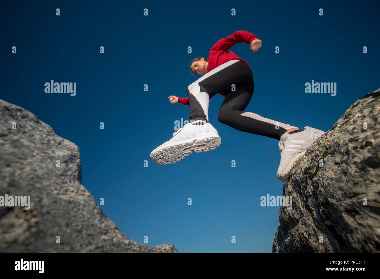 woman jumping across rocks, photographed looking up. Stock Photo