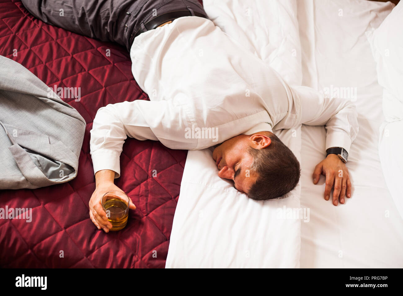 Businessman sleeping on a bed, holding glass of whiskey Stock Photo Alamy