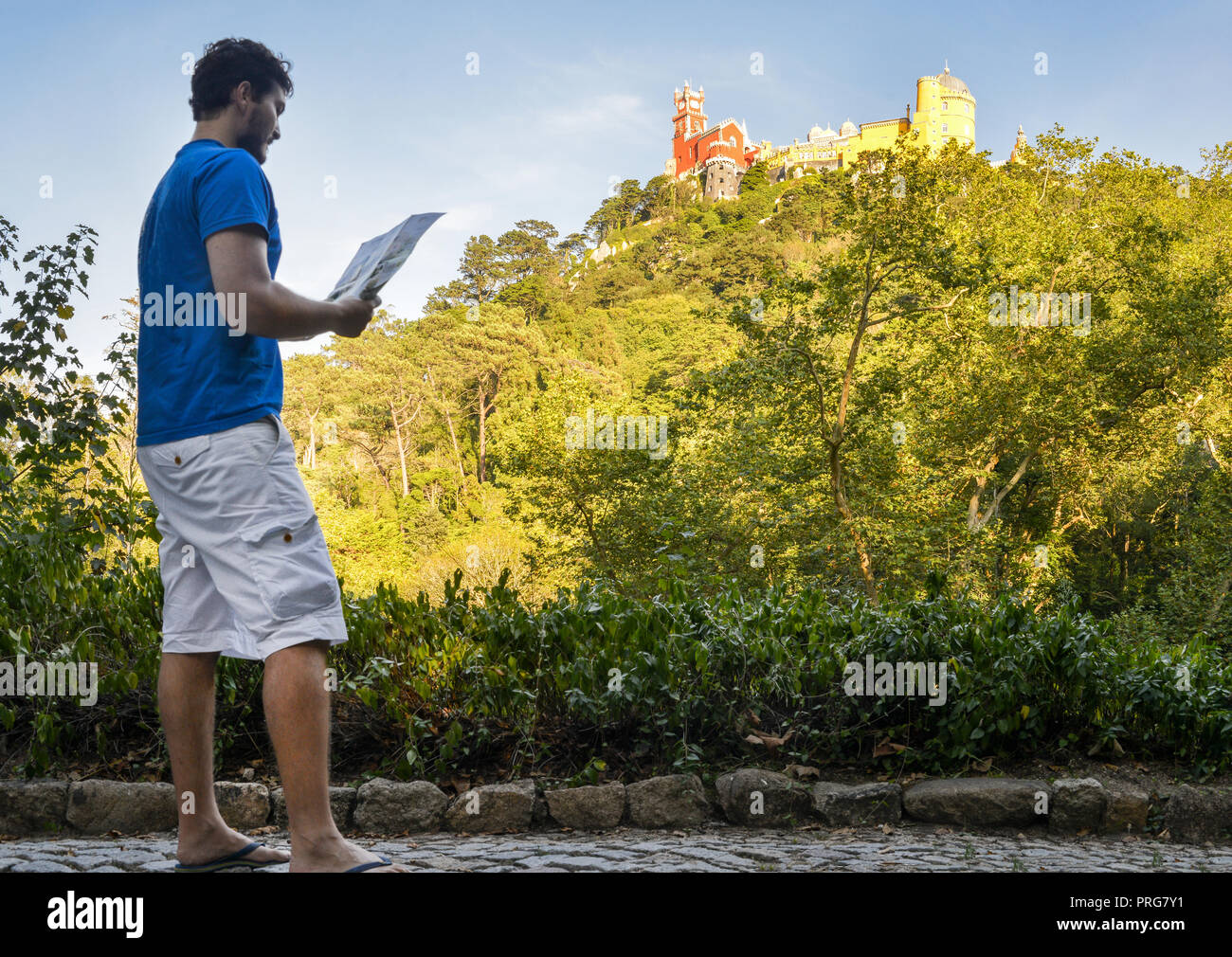 Young man (20-25) tourist holding a map while looking up at the Pena National Palace, a Romanticist palace in Sao Pedro de Penaferrim, Sintra Portugal Stock Photo