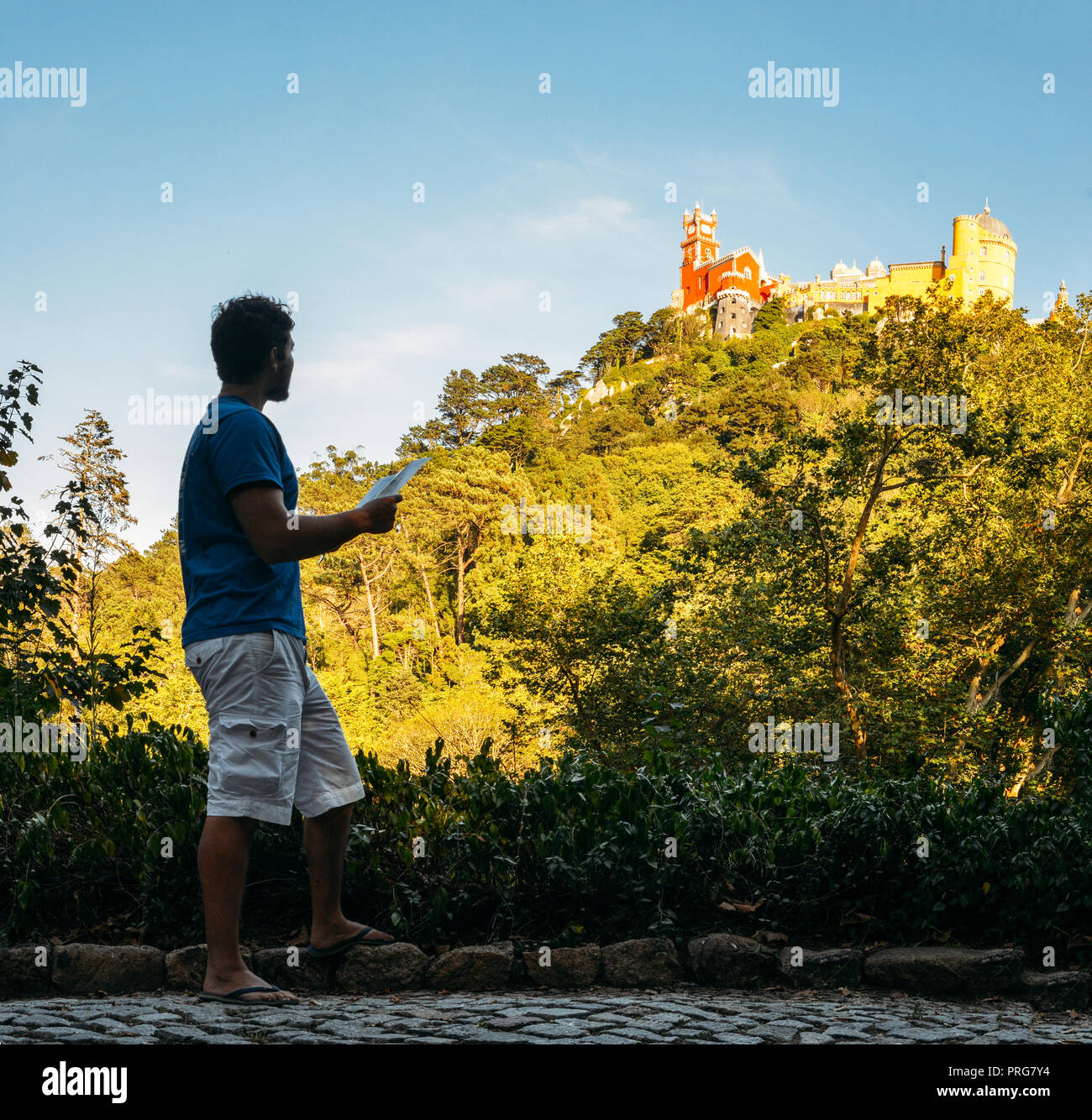 Young man (20-25) tourist holding a map while looking up at the Pena National Palace, a Romanticist palace in Sao Pedro de Penaferrim, Sintra Portugal Stock Photo