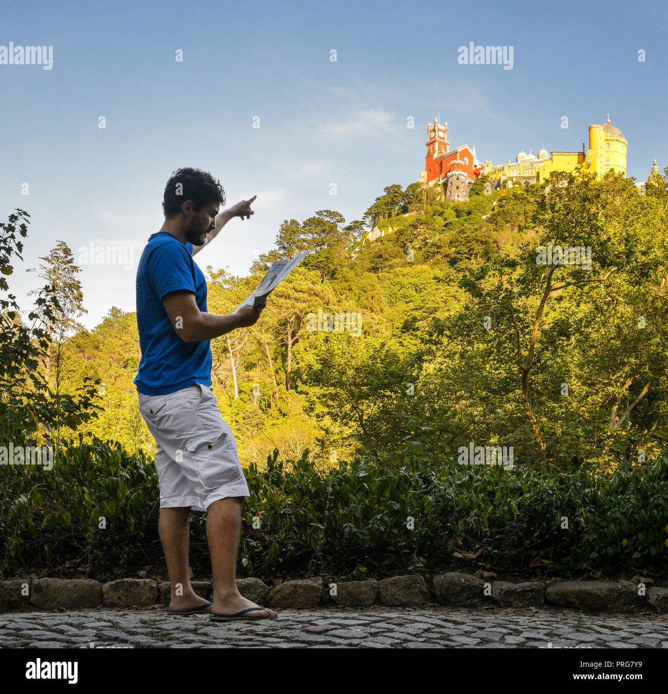Young man (20-25) tourist holding a map while pointing towards the Pena National Palace, a Romanticist palace in Sao Pedro de Penaferrim, Sintra Stock Photo