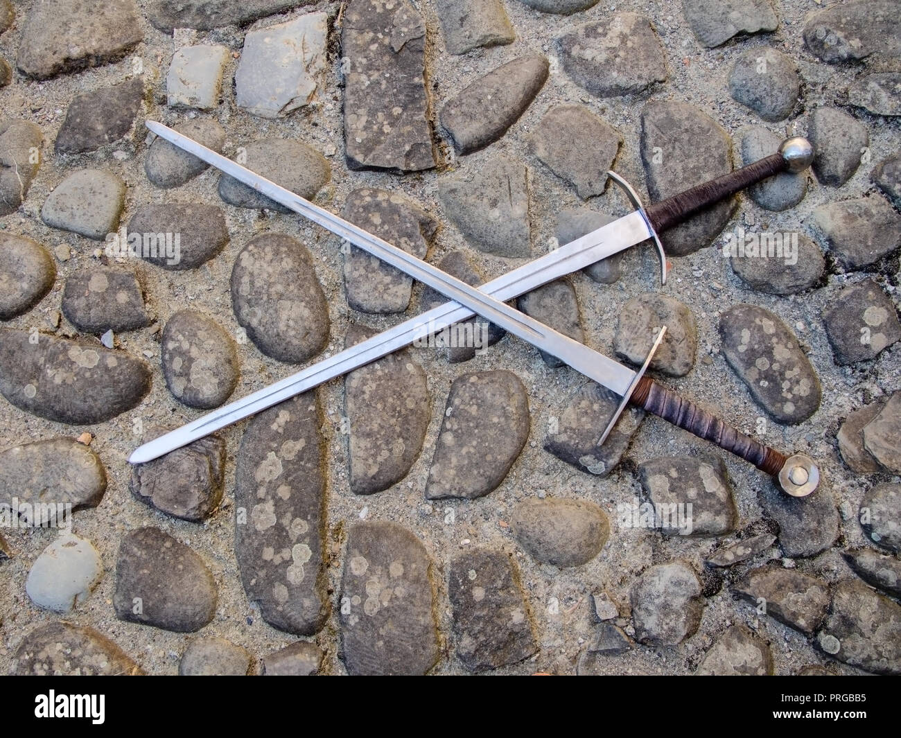 Two medieval swords, crossed, on cobblestone floor. Stock Photo