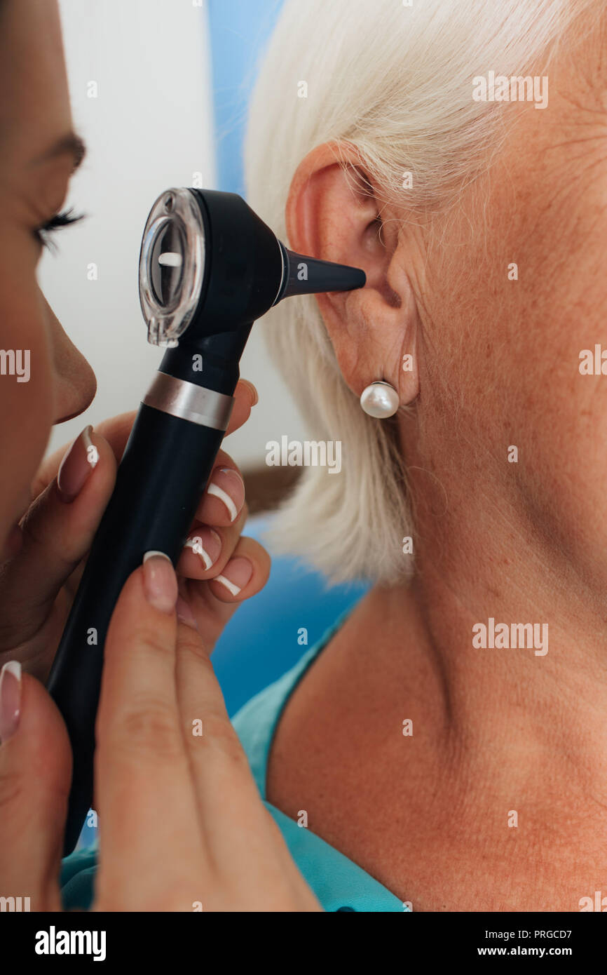 Doctor examining senior female ear with otoscope Stock Photo