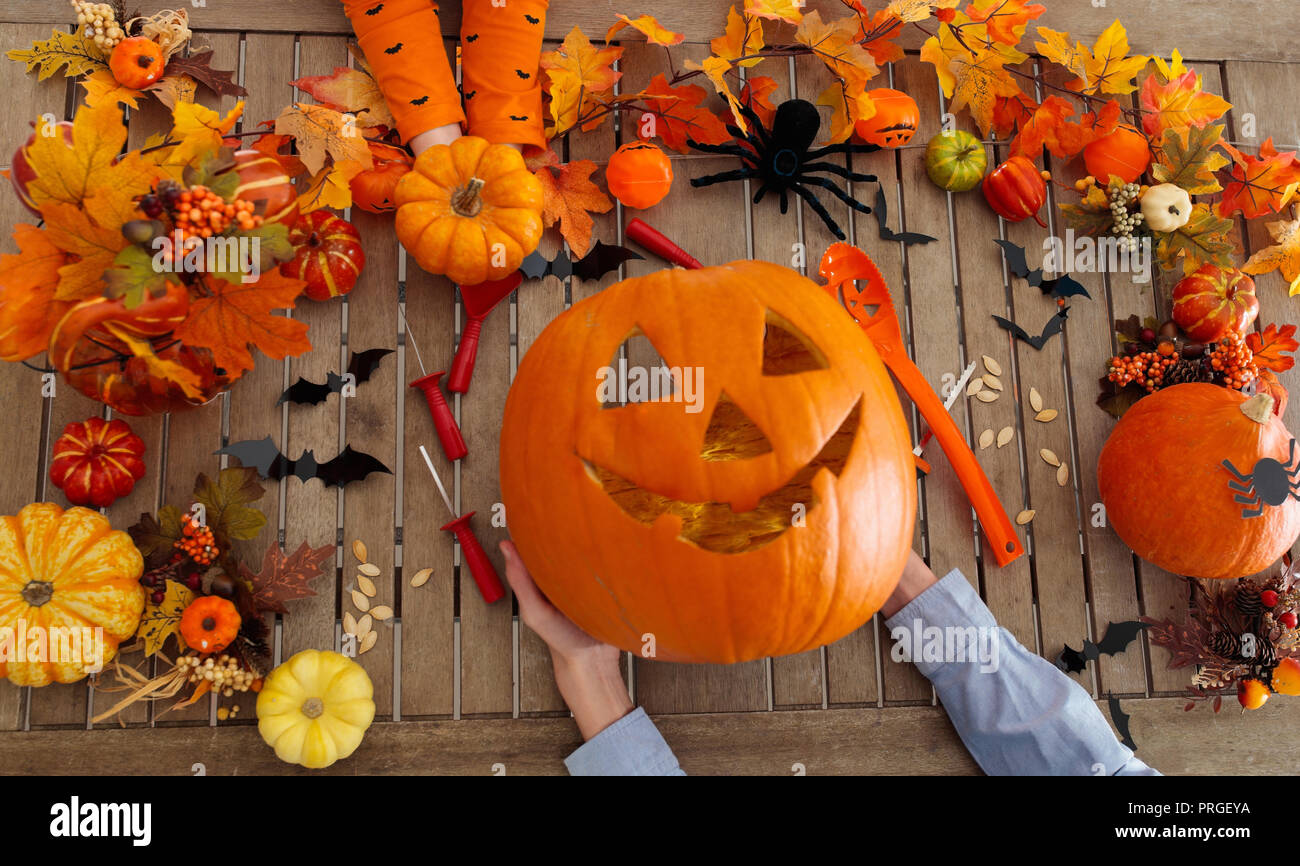 Family carving Halloween pumpkin on wooden table with autumn leaves decoration. Top view flat lay of hands and carved pumpkins. Halloween trick or tre Stock Photo