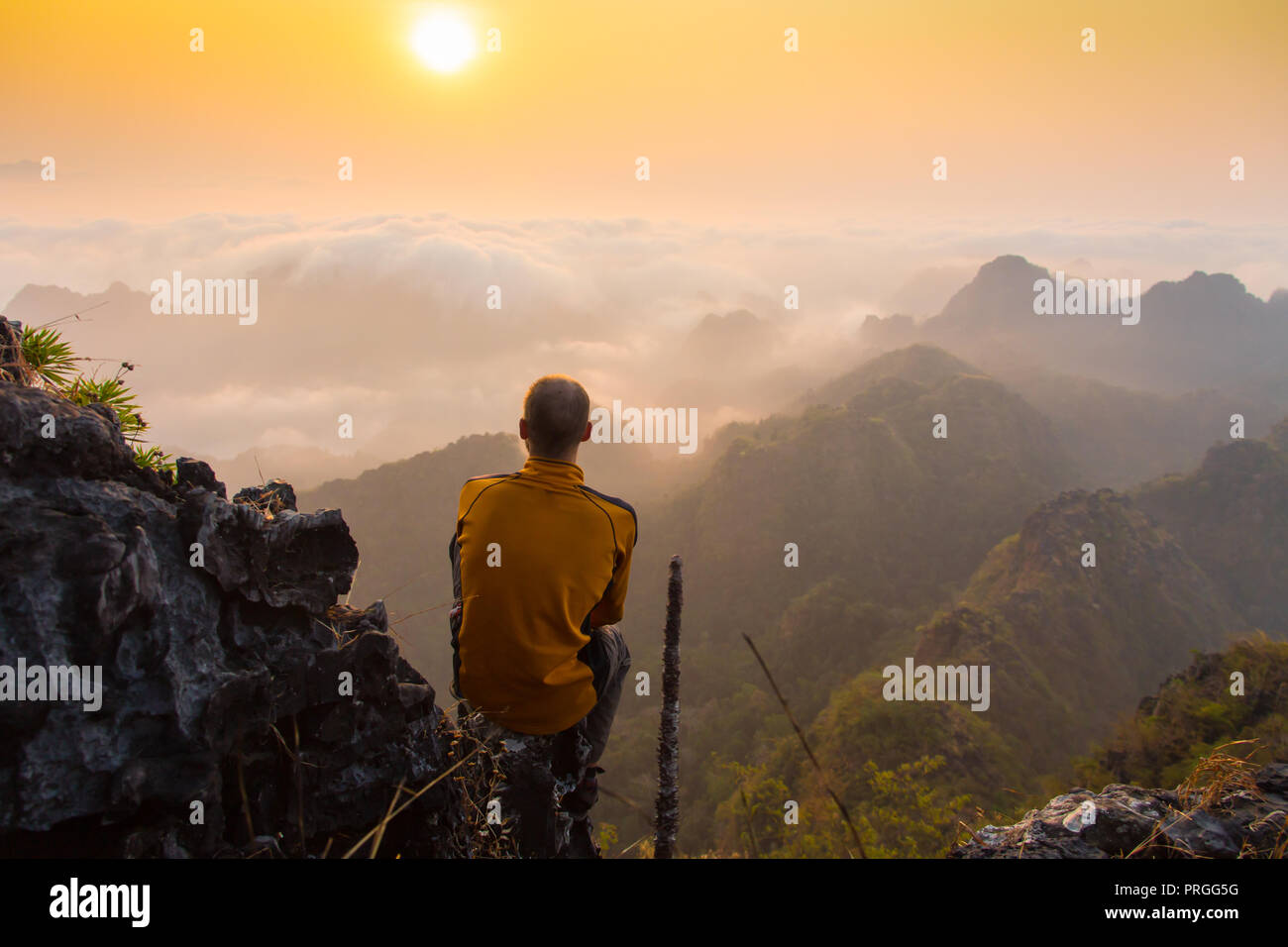 man sitting on stone top of high mountain Stock Photo - Alamy
