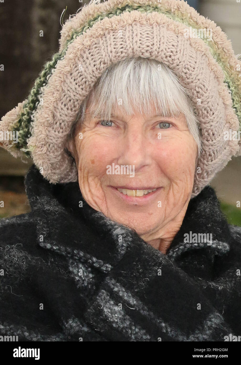 Retired lady enjoying sitting outside with winter coat and woolly hat on. Stock Photo