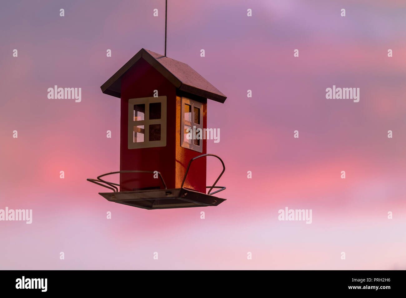 Small red typical Swedish or Scandinavian wood house looking bird house against beautiful pink sunrise sky Stock Photo