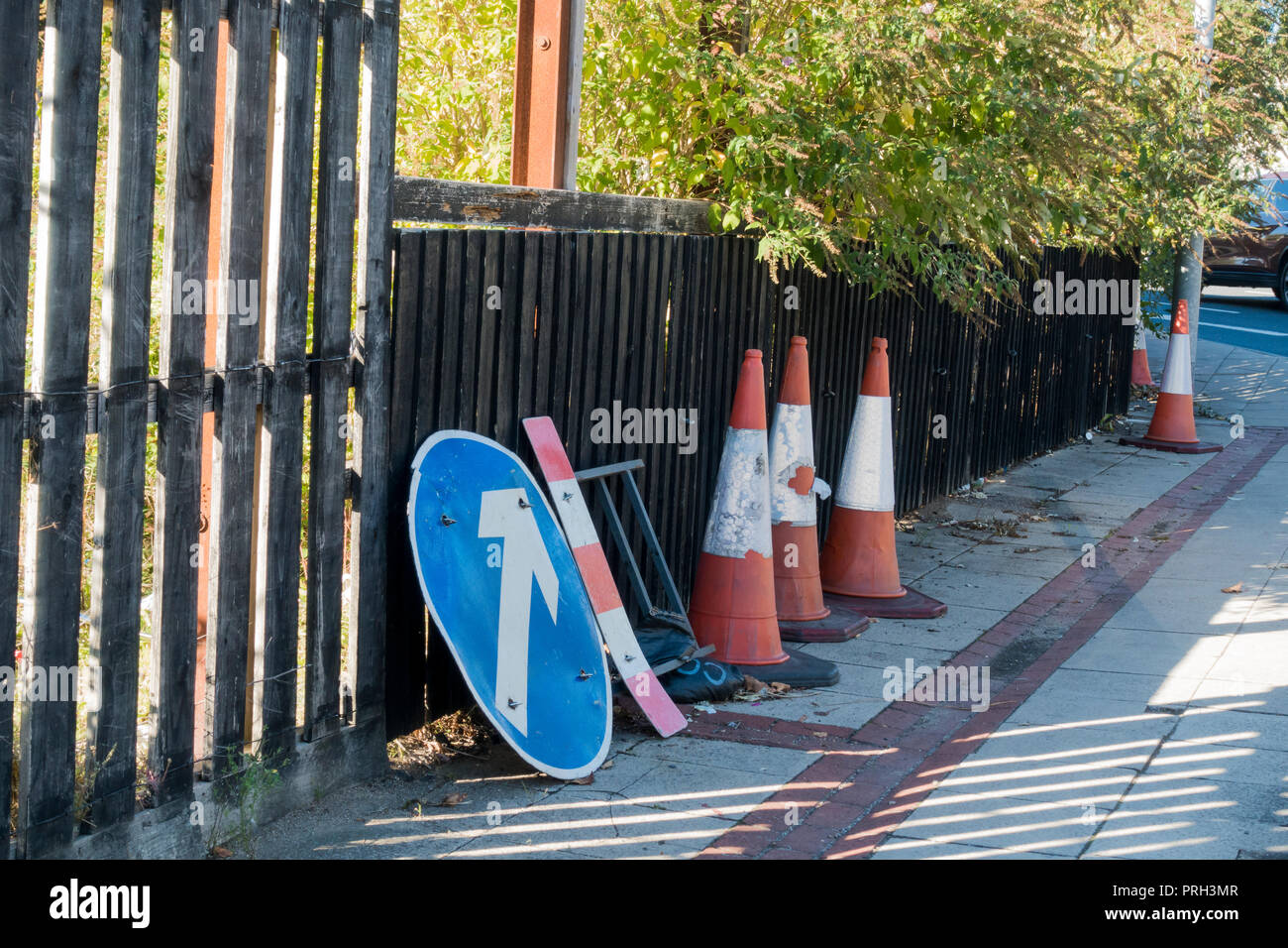 Road traffic cones and a blue circle roadsign symbol, not in use, on the pavement beside a wooden fence,  UK Stock Photo