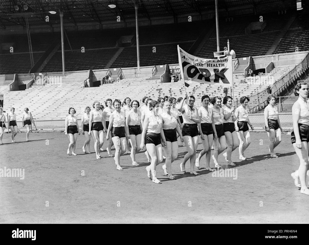 Members of The Women's League of Health and Beauty, marching inside a large sports stadium in England during the 1930s. Banners from the branch at York is visible. They are campaigning about Racial Health Stock Photo