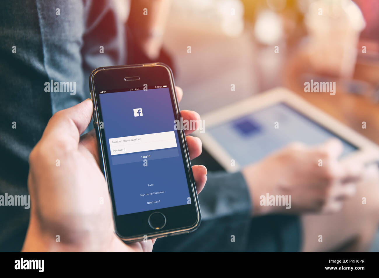 Facebook App on iPhone with people using tablet background closeup male hand hold social network on smart device concept.23 September 2018,Bangkok Tha Stock Photo