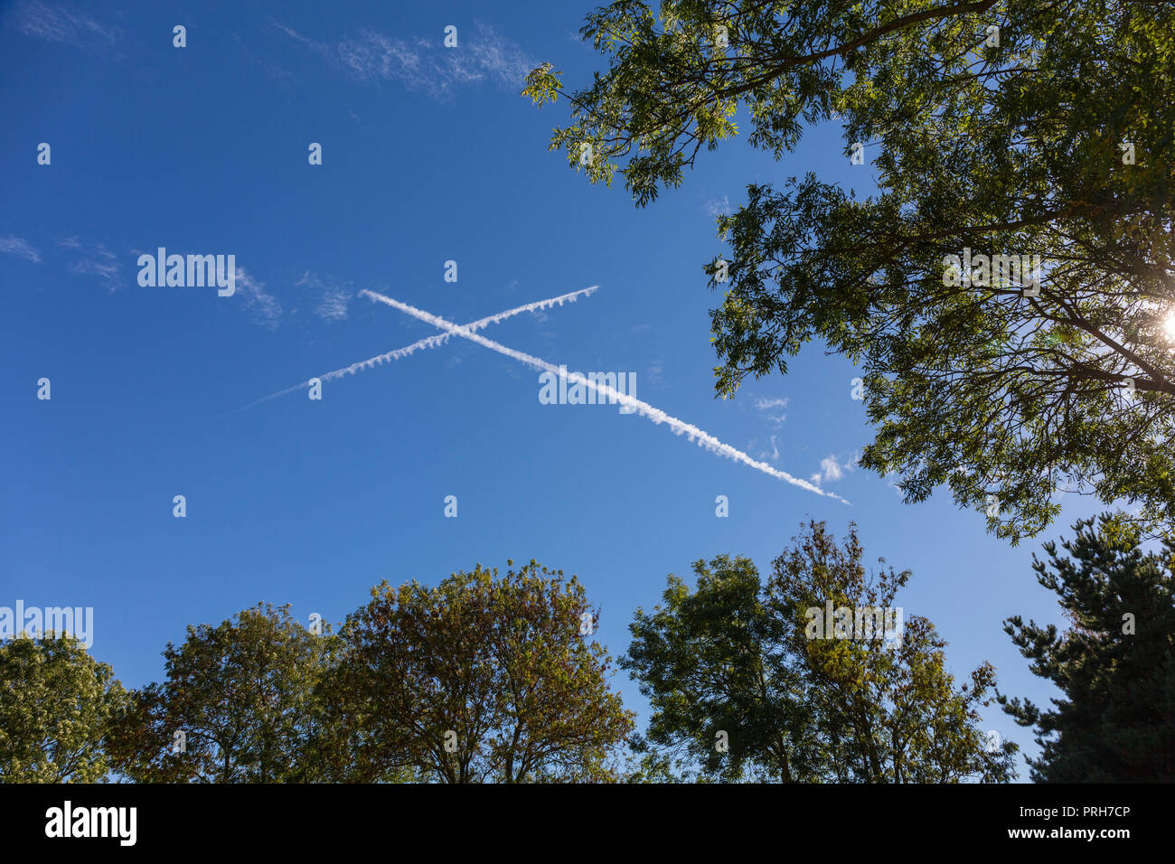 Vapour trails from two aeroplanes make an X cross in a blue sky over Suffolk, UK. Stock Photo
