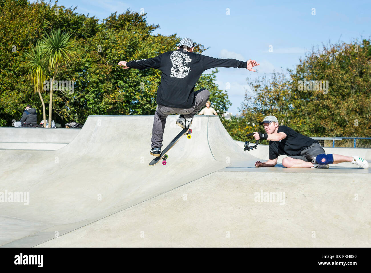A skateboarder being filmed performing an aerial trick at Concrete Waves Skateboard Park in Newquay in Cornwall. Stock Photo