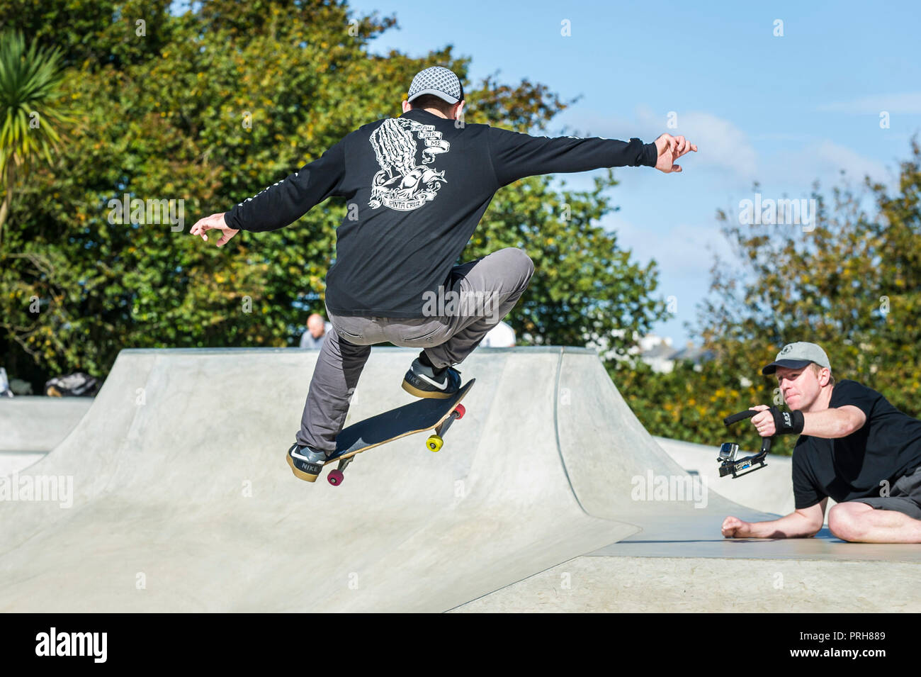 A skateboarder being filmed performing an aerial trick at Concrete Waves Skateboarding Park in Newquay in Cornwall. Stock Photo