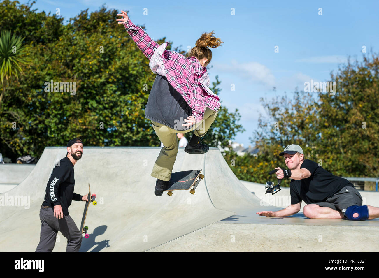 A female skateboarder being filmed performing an aerial trick at Concrete Waves Skateboarding Park in Newquay in Cornwall. Stock Photo