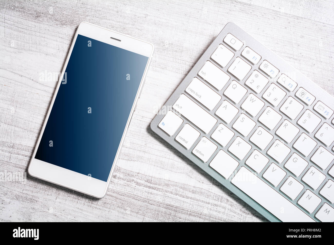 Mobile With Reflection Lying Next To A White Keyboard On A Table Stock Photo