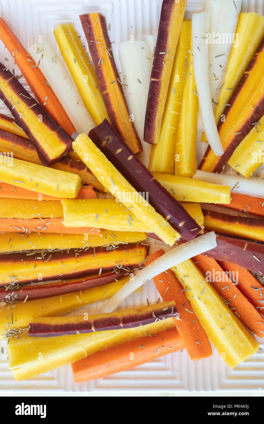 Colorful yellow, orange, red and white sliced raw carrots plated and sprinkled with dry Rosemary heb Stock Photo