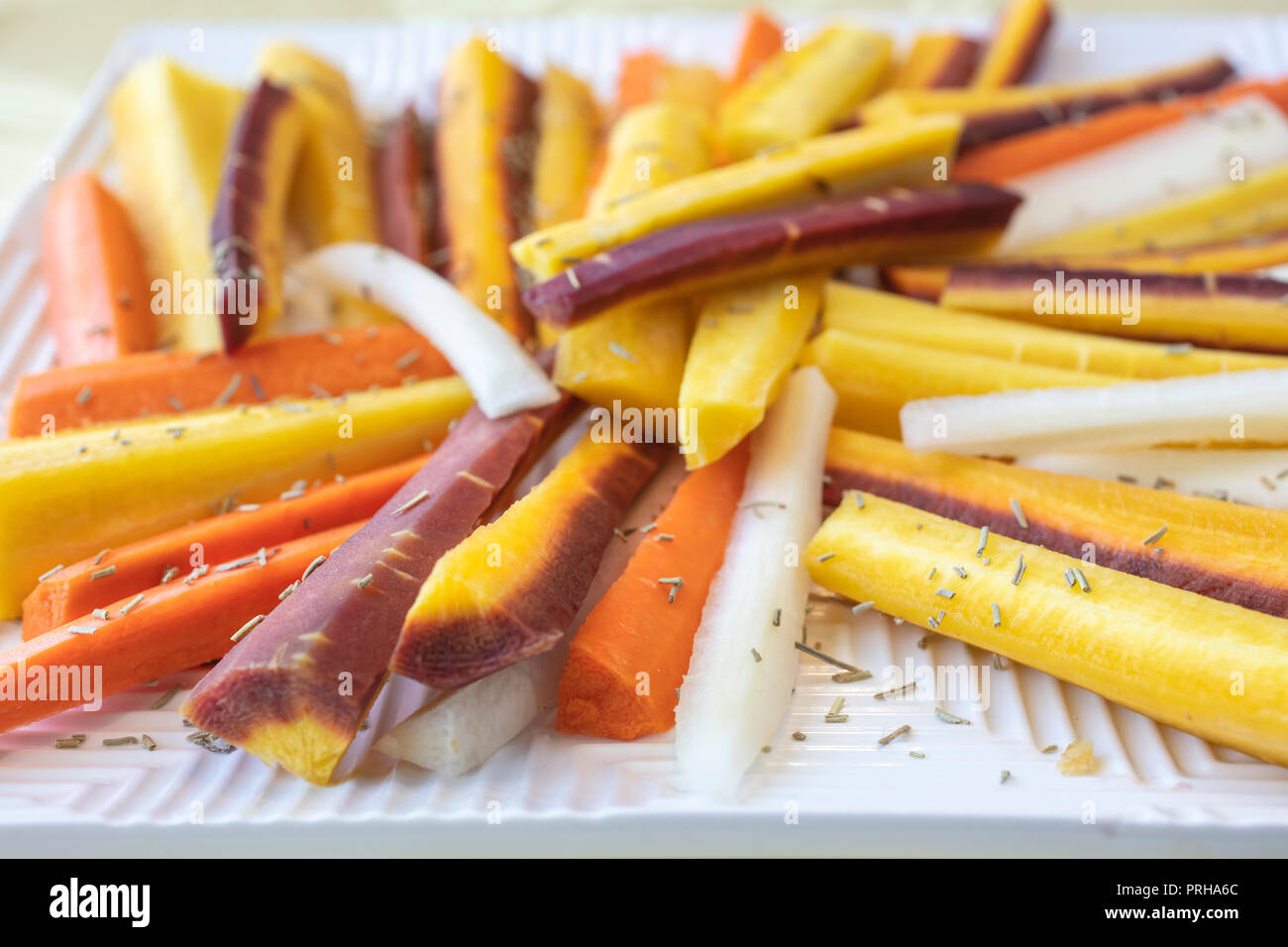 Colorful yellow, orange, red and white sliced raw carrots plated and sprinkled with dry Rosemary heb Stock Photo