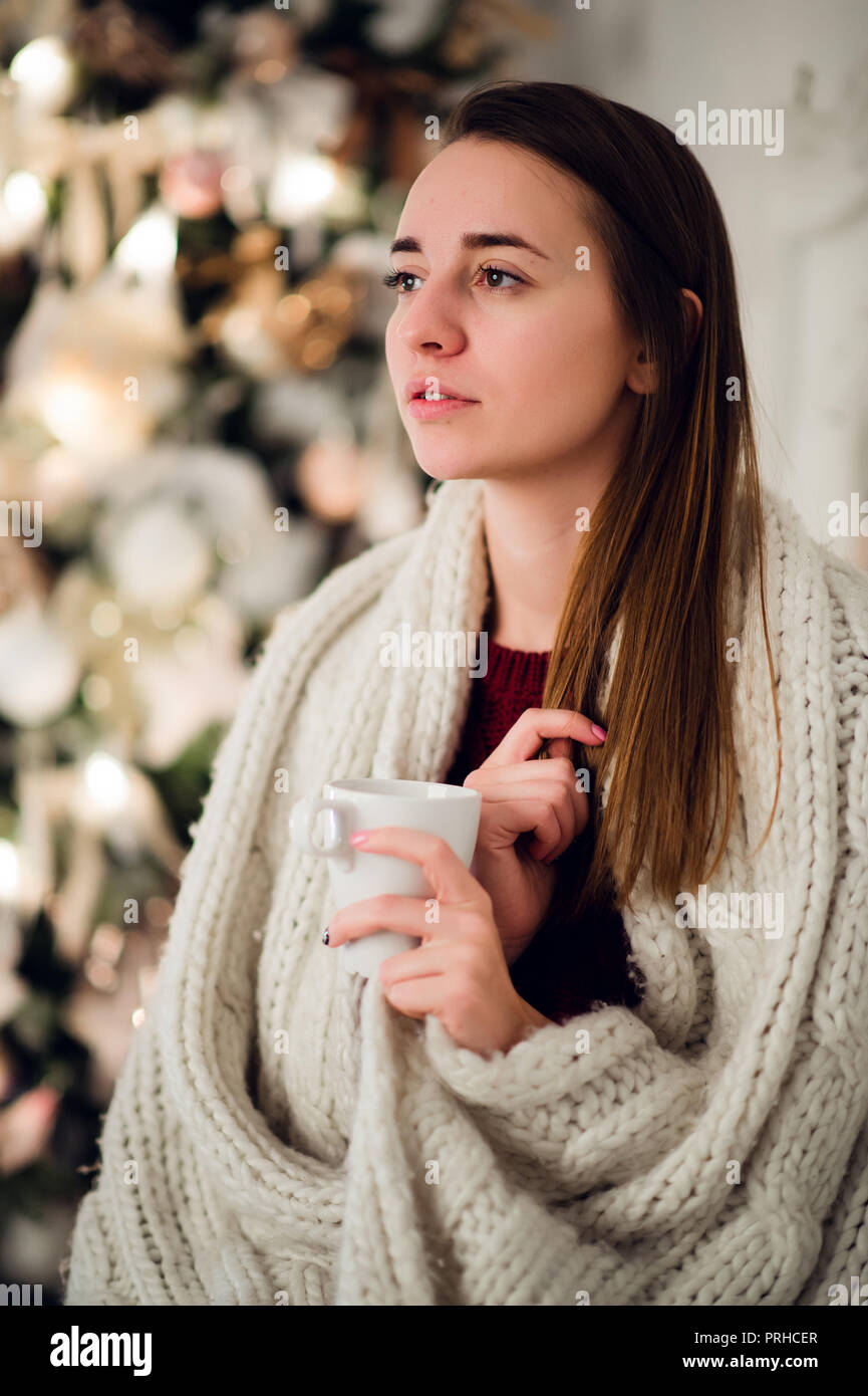 Young woman relaxing with a mug of coffee as she cuddles up in warm