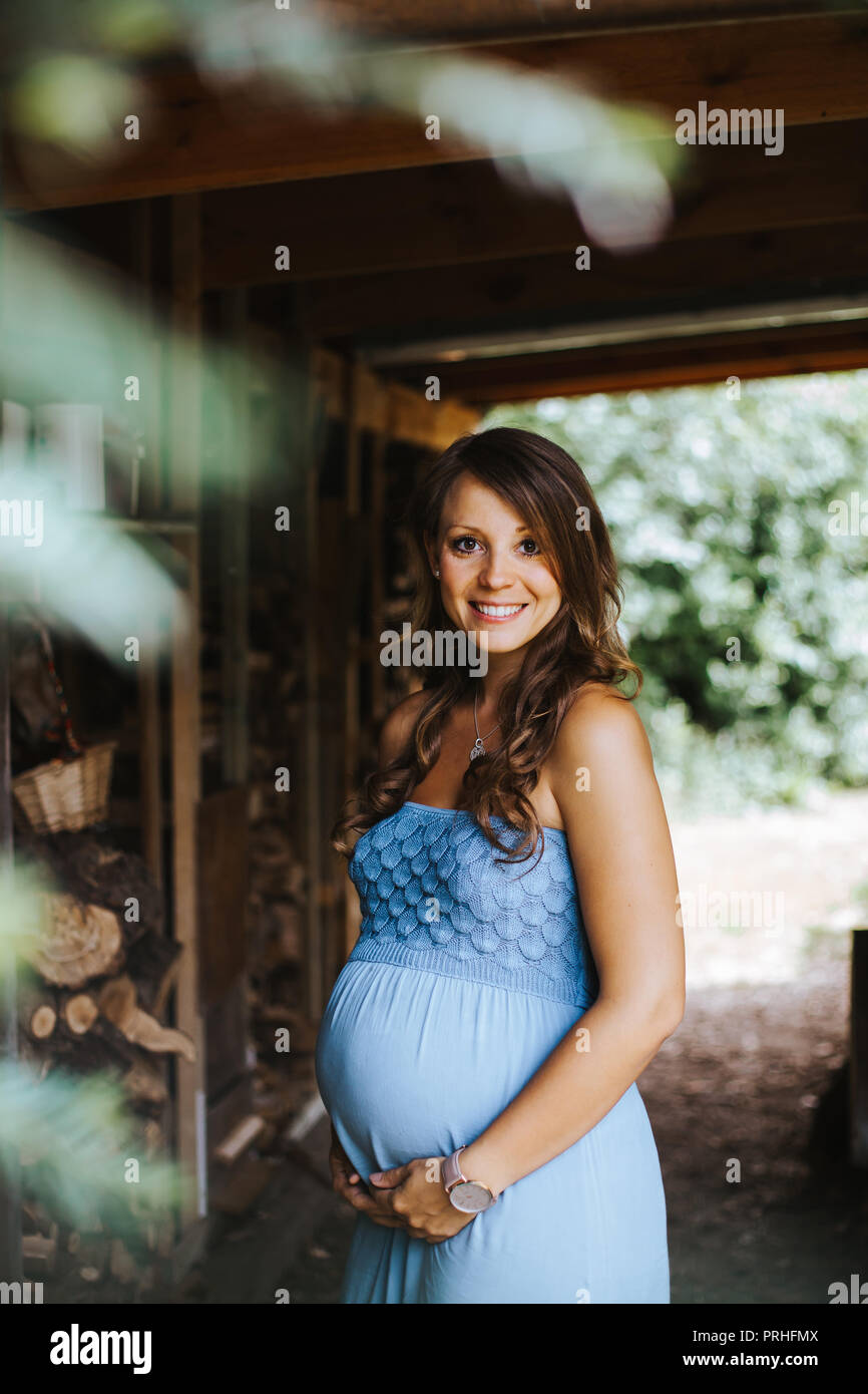 portrait of beautiful pregnant woman in blue dress holding her belly ...