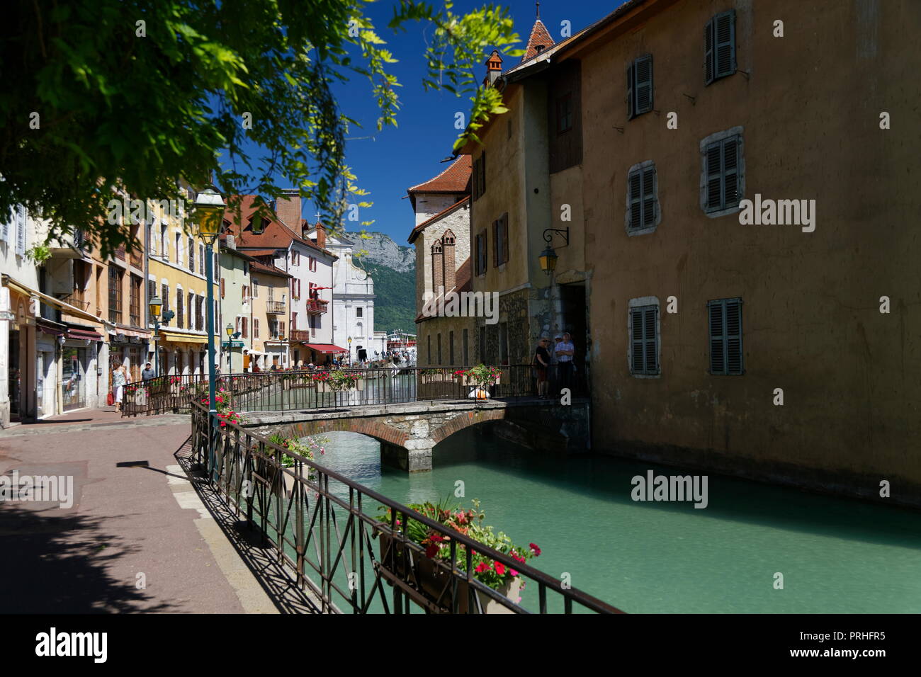 Shops and cafes framed through tree foliage on the canals of Annecy France Stock Photo