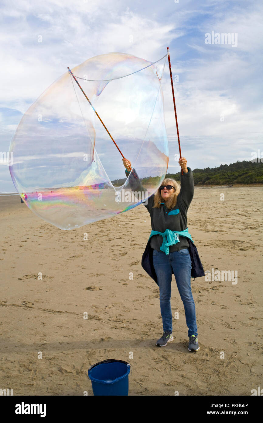 A senior woman using a bubble wand to creaate huge soap bubbles at a bubble blowing festival on the beach near Yachats, oregon Stock Photo