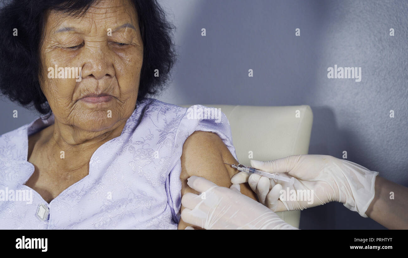 Doctor giving vaccine injection into senior woman shoulder Stock Photo