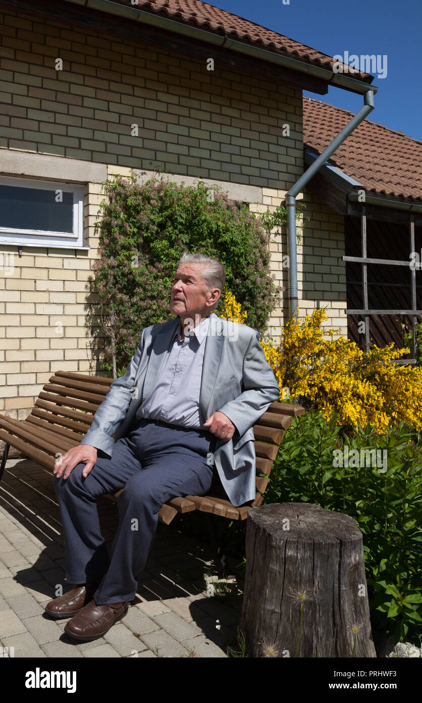 Happy old man is sitting on a bench in his yard at the house Stock ...
