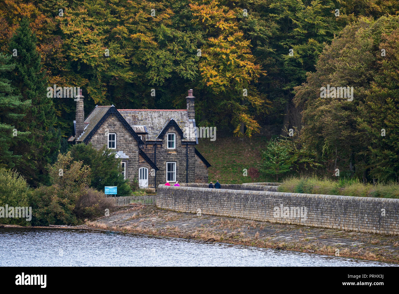 Stone-built house standing at woodland edge, by embankment wall & on shore of lake - Fewston Reservoir, Washburn Valley, North Yorkshire, England, UK. Stock Photo