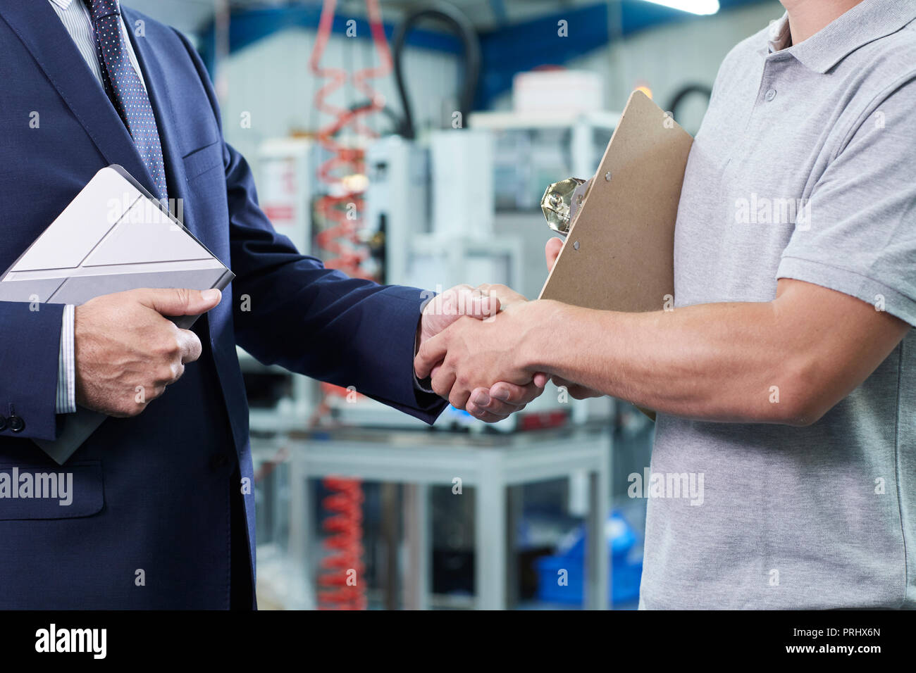 Close Up Of Business Owner With Digital Tablet In Factory Shaking Hands With Engineer Stock Photo
