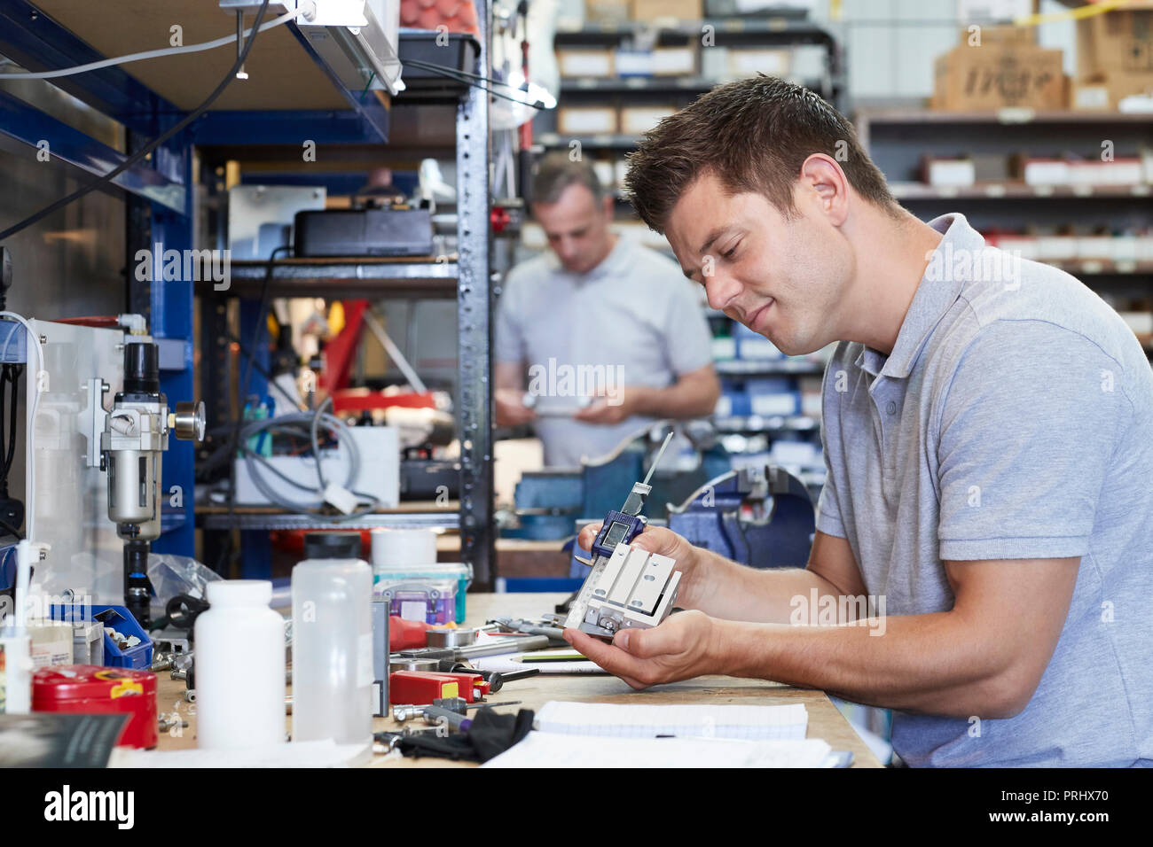 Engineer In Factory Measuring Component At Work Bench Using Micrometer Stock Photo
