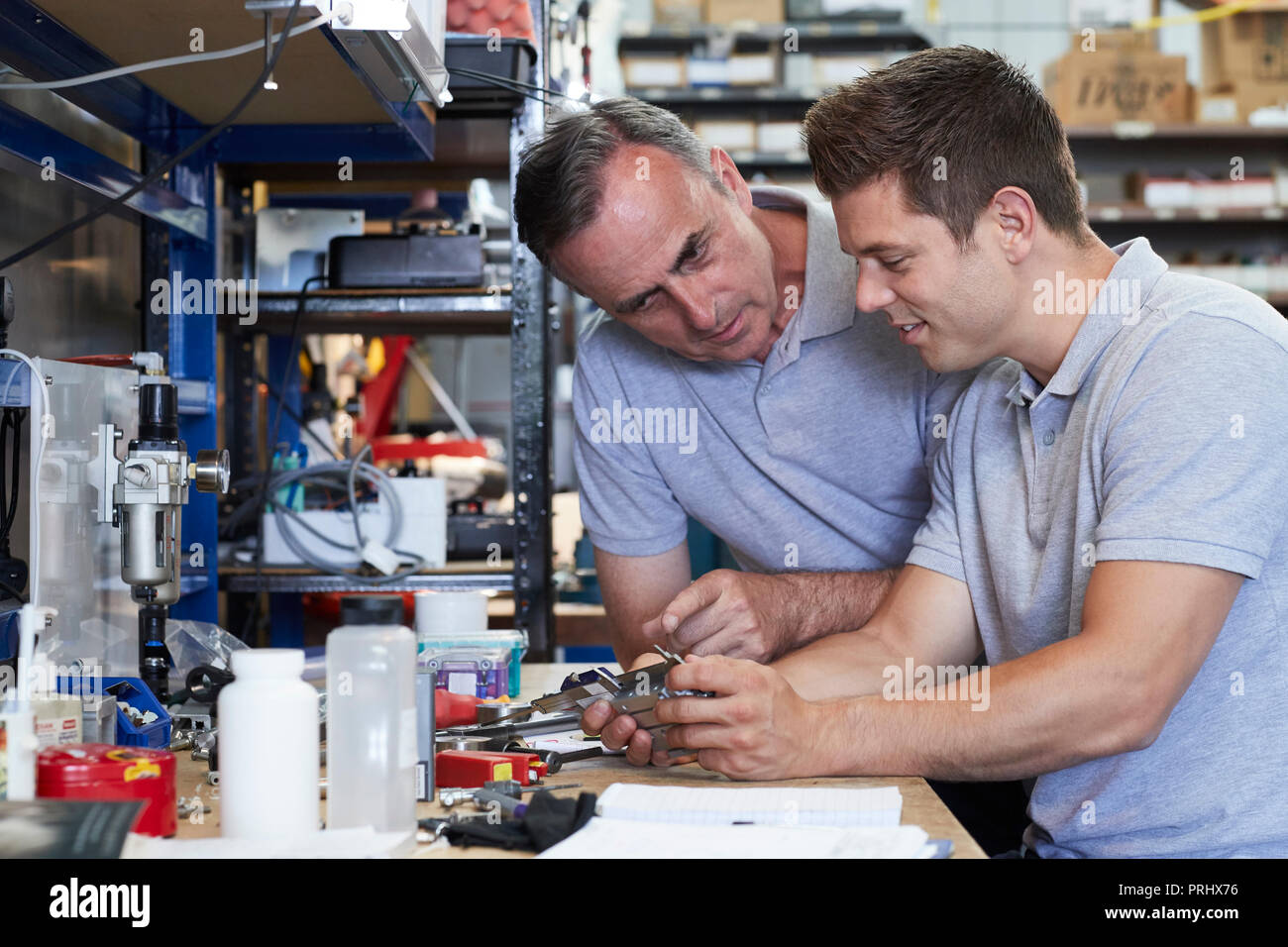 Engineer Helping Male Apprentice In Factory To Measure Component Using Micrometer Stock Photo