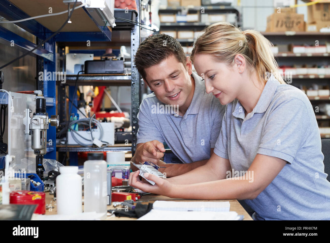 Engineer Helping Female Apprentice In Factory To Measure Component Using Micrometer Stock Photo