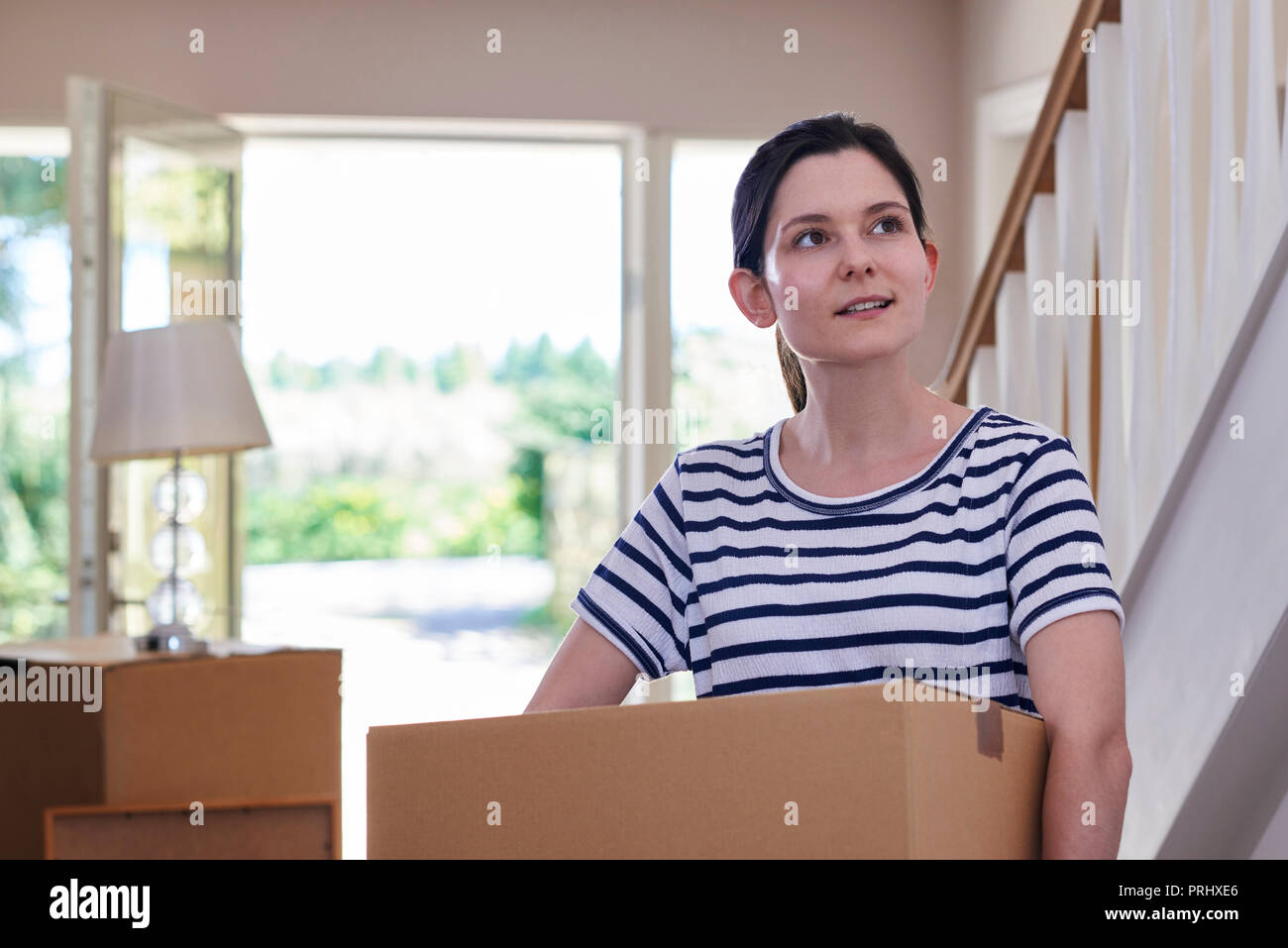 Young Woman Carrying Boxes Into New Home On Moving Day Stock Photo