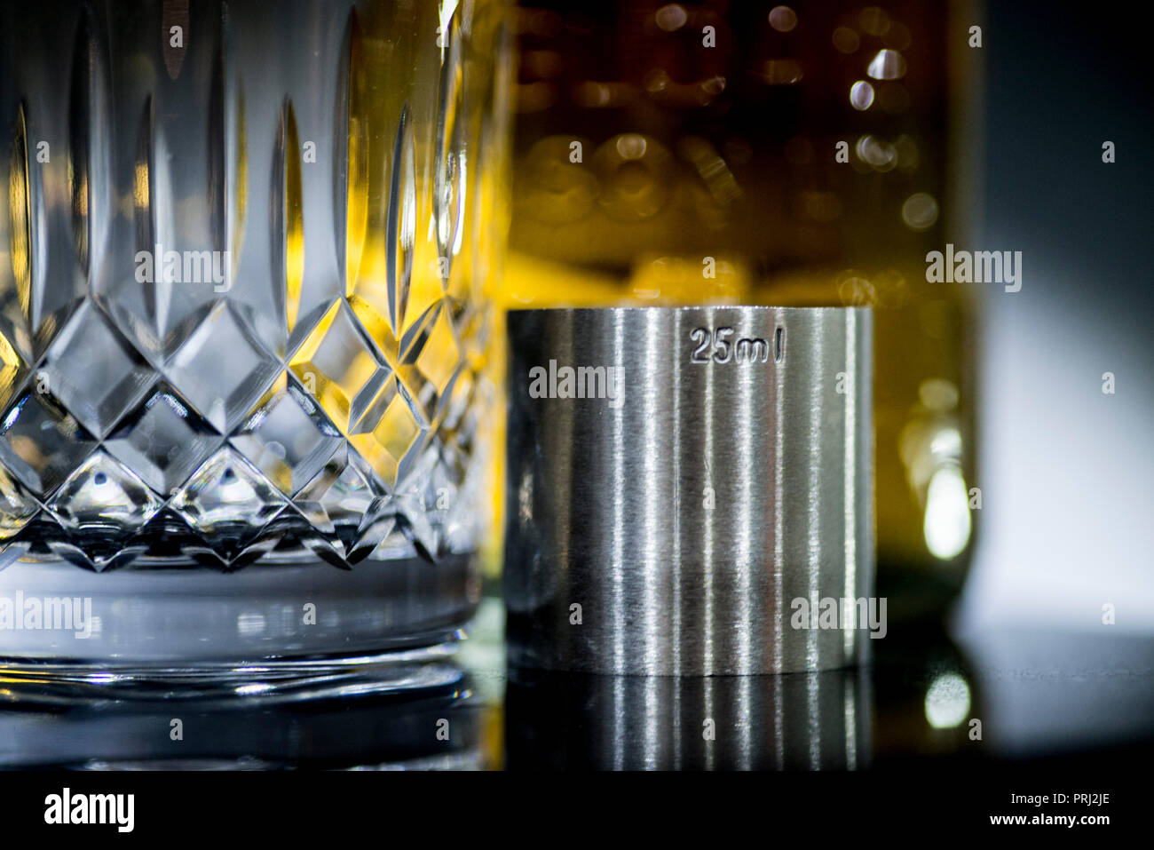 Whisky glass and spirit measure with out of focus whisky bottle in the background. Stock Photo