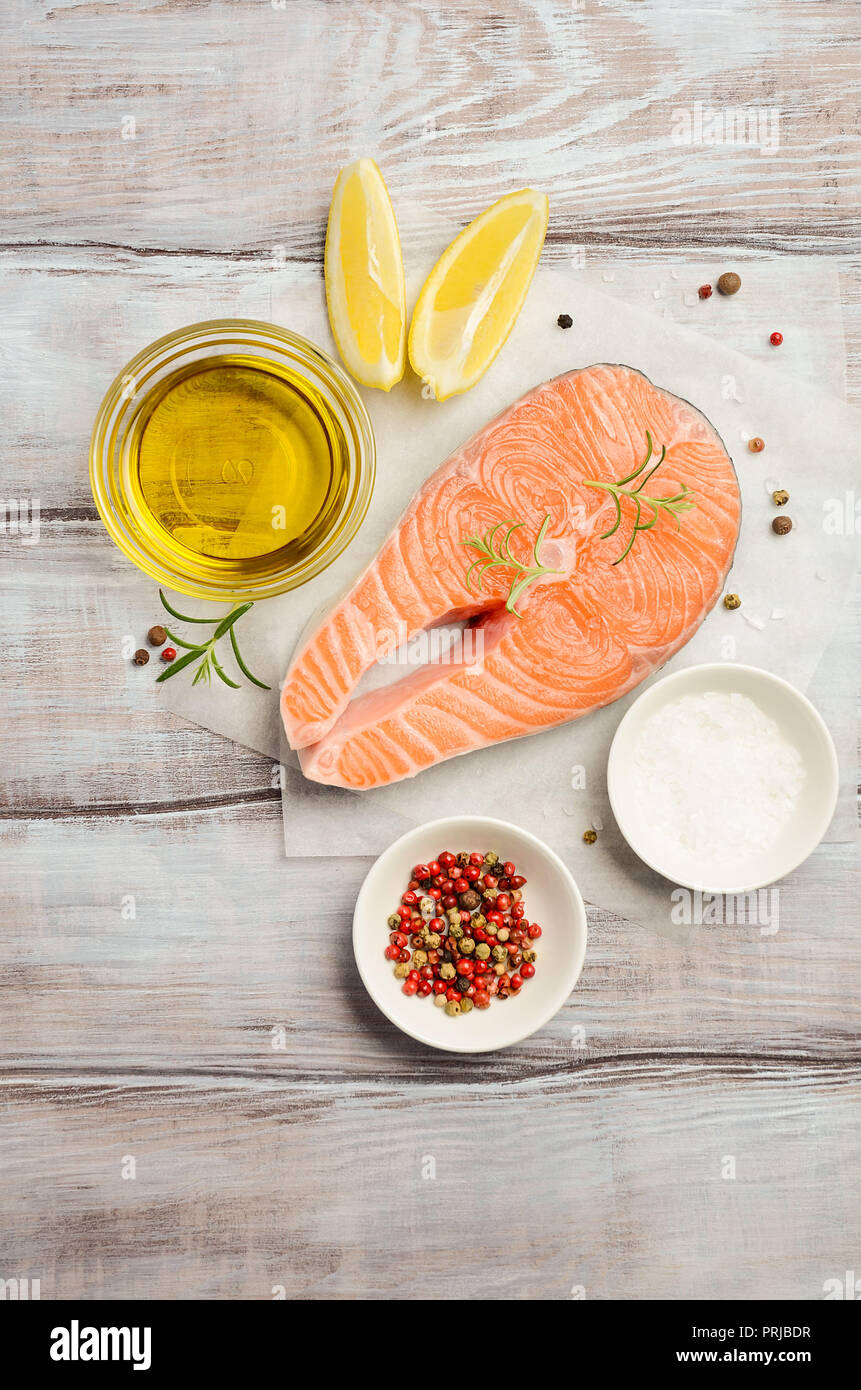 Fresh raw salmon steak with lemon, olive oil and spices on rustic wooden background. Ingredients for making healthy dinner. Healthy diet concept. Stock Photo