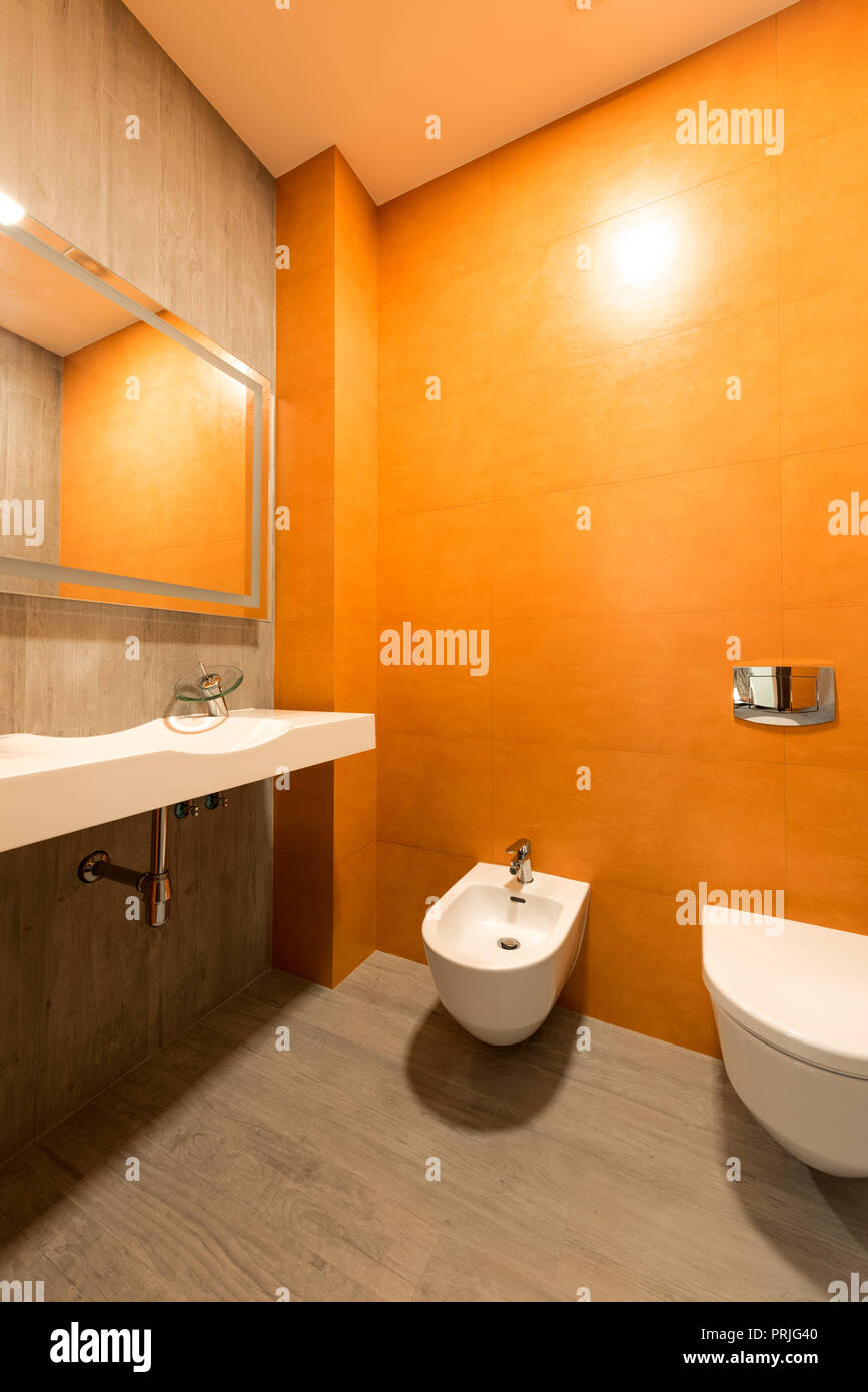 interior of modern bathroom in orange and white colors with toilet and