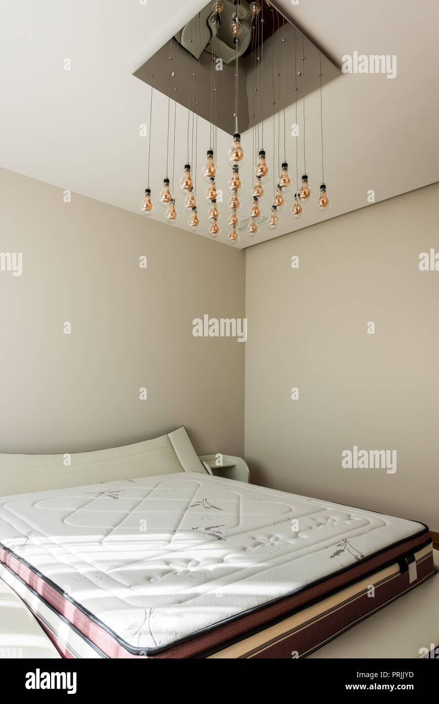 interior of stylish bedroom with bed and light bulbs on ceiling Stock Photo