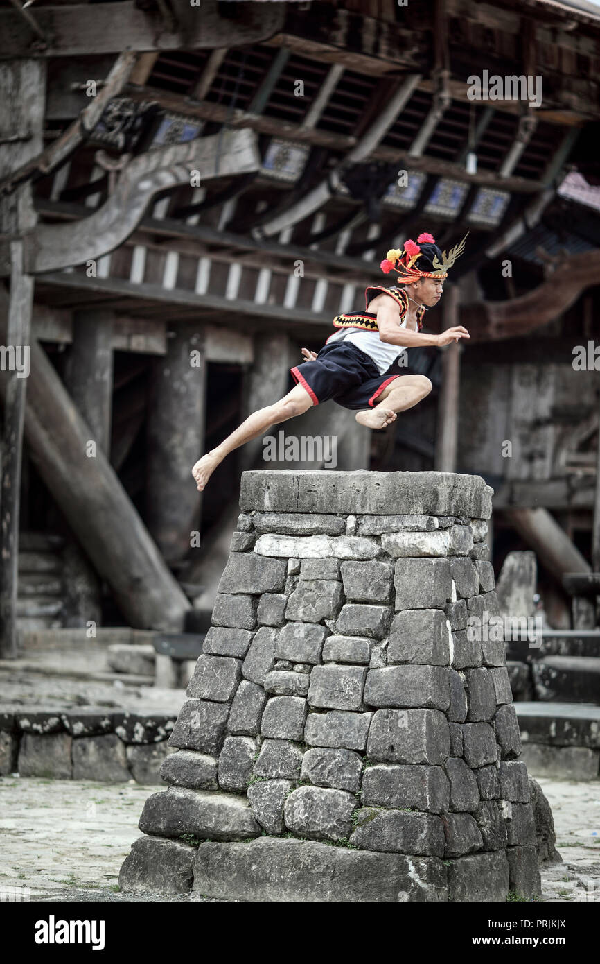 Man in traditional attire stone jumping over rock platform on Nias Island, Sumatra, Indonesia Stock Photo