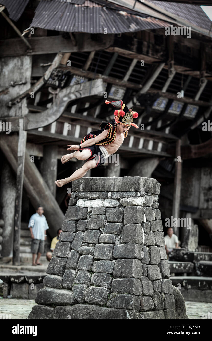 Man in traditional attire stone jumping over rock platform on Nias Island, Sumatra, Indonesia Stock Photo